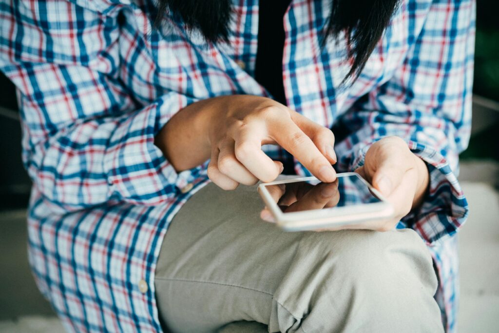 Eine Person sitzt und tippt auf ihr Handy.