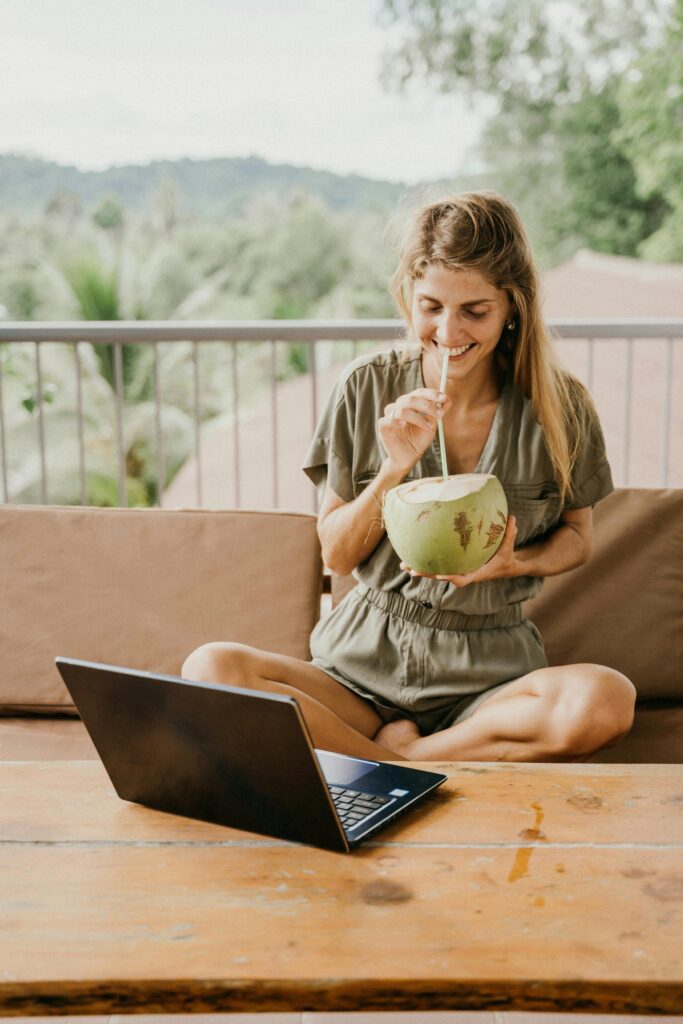 Eine Frau sitzt vor ihrem Laptop zum arbeiten und trinkt aus einer Kokosnuss