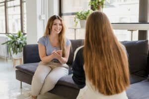 Eine Frau sitzt mit einer anderen Frau auf einem Sofa und spricht mit ihr in Gebärdensprache