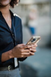 Person hält ein Smartphone in beiden Händen und schaut darauf, Nahaufnahme von Händen und Oberkörper.